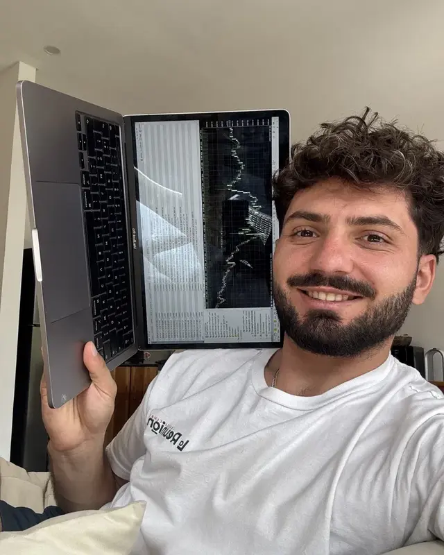 Flo smiling, holding up a laptop that shows a trading chart